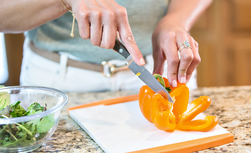 Close up image of a blogger cutting up an orange pepper with salad greens nearby.