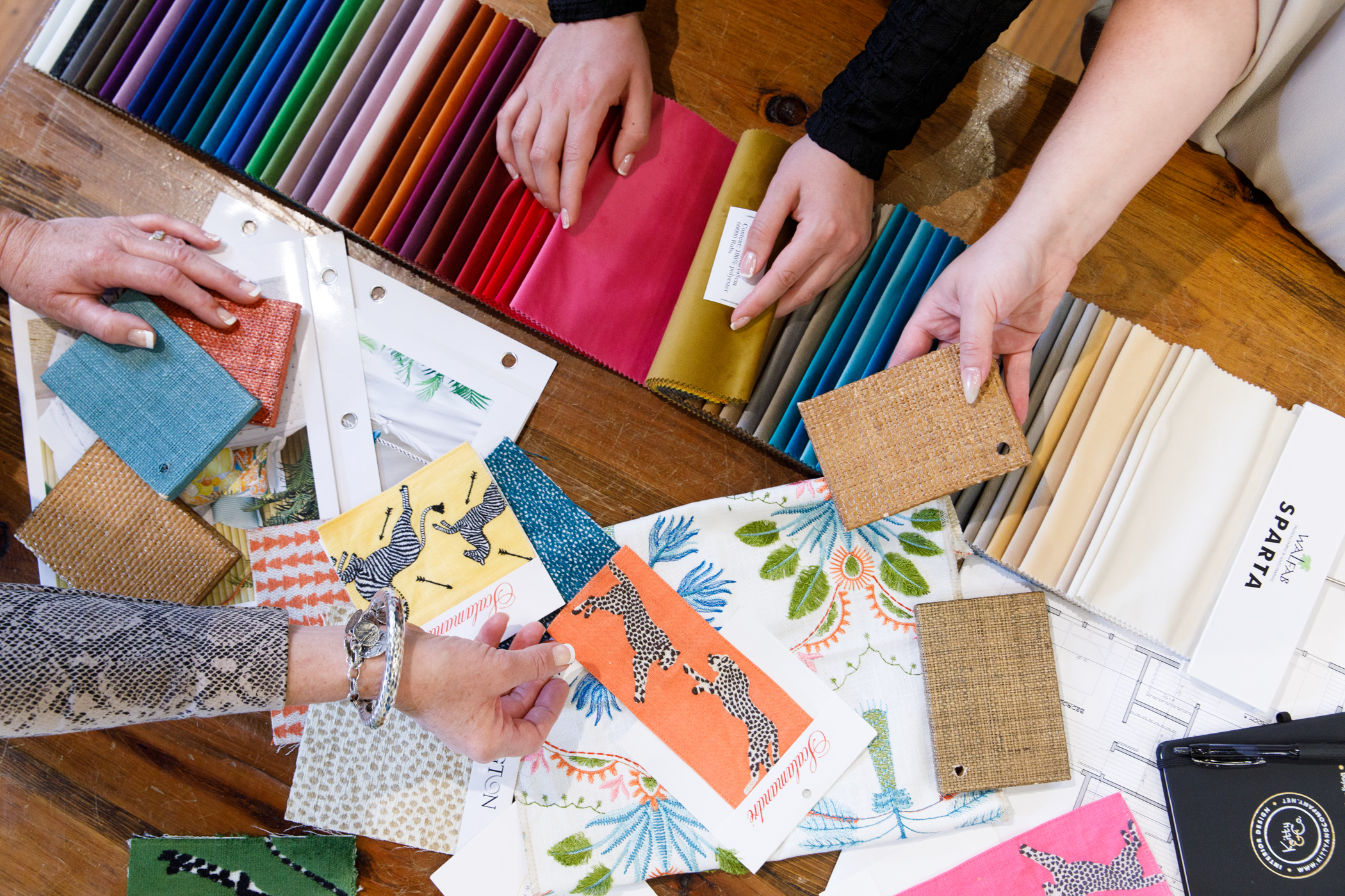 A scene photographed from the top down of several hands looking at fabric at an interior design studio.