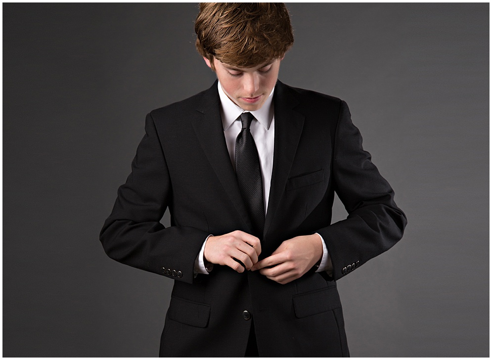 studio portrait of a senior guy buttoning his jacket in a suit and tie look.