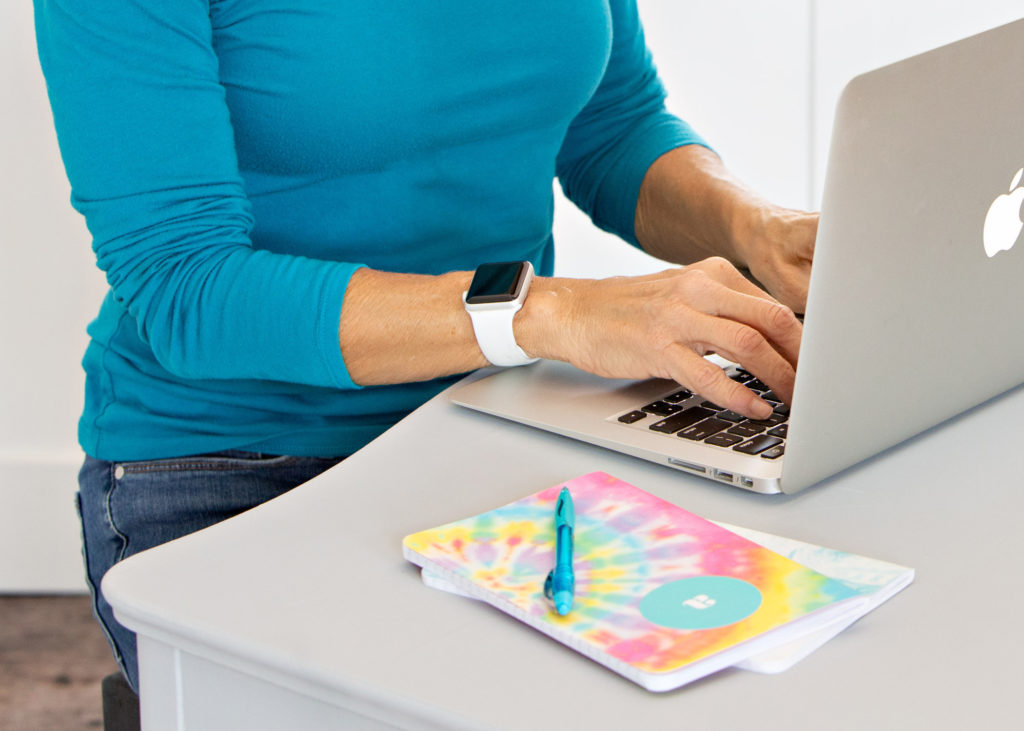 Close up of a woman on a laptop wearing a turquoise shirt and an Apple watch